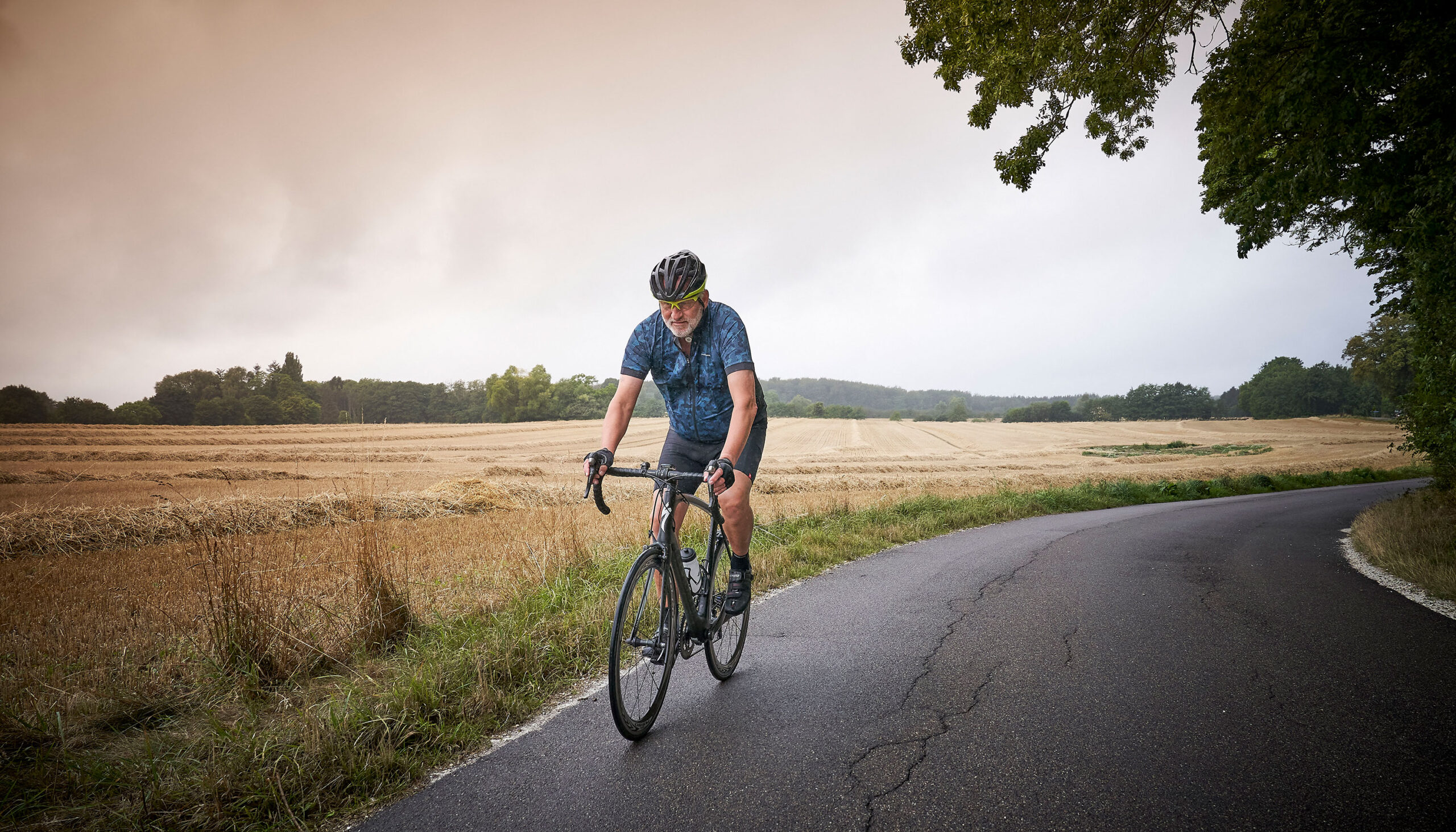 Man with a neck stoma biking next to a meadow.