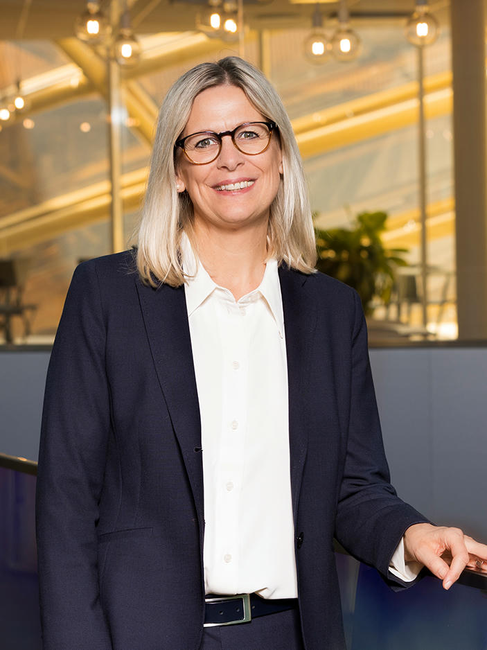 Stefanie Schmitz in suit, wearing glasses, smiling.